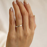 Hand wearing a 2mm wide brushed flat white gold wedding ring on a neutral background