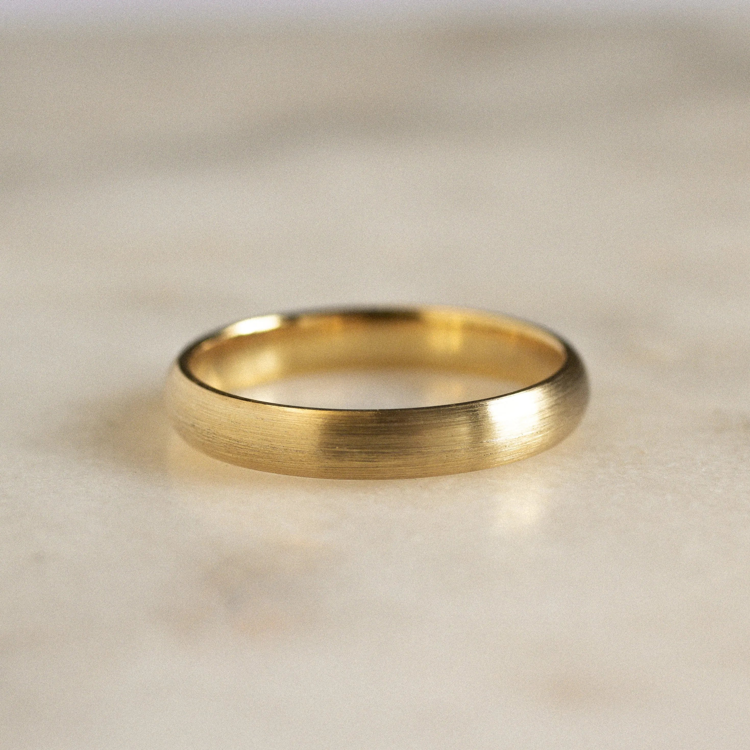gold wedding band with brushed texture on marble surface