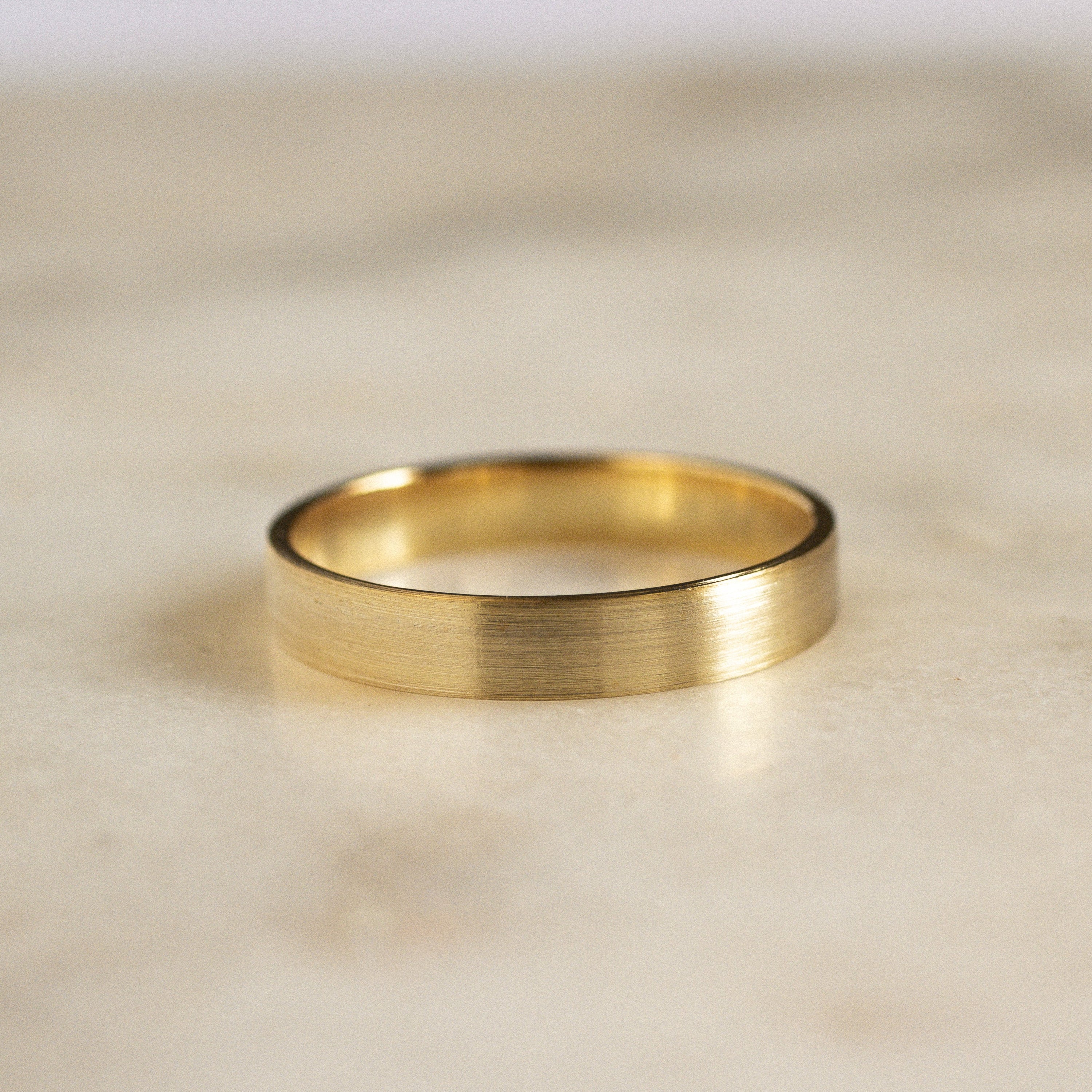 gold flat wedding ring with brushed finish on marble surface