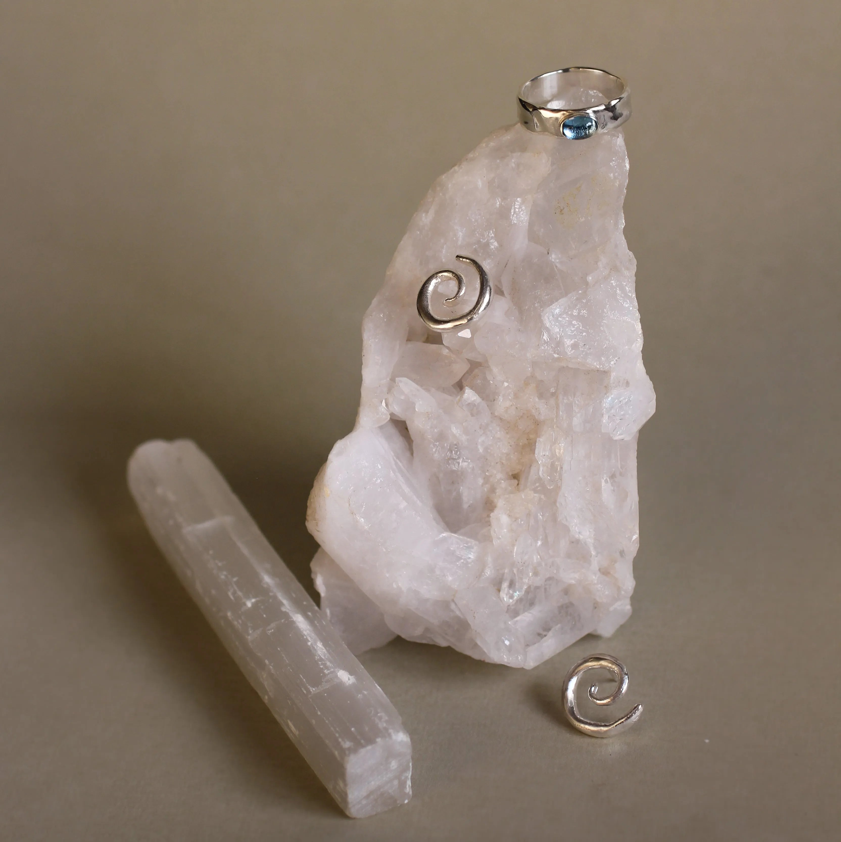 crystals with spiral silver earrings and silver blue topaz ring with beige background