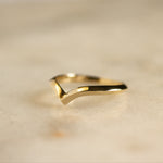v shaped gold wedding ring on marble surface in angular knife edge shape