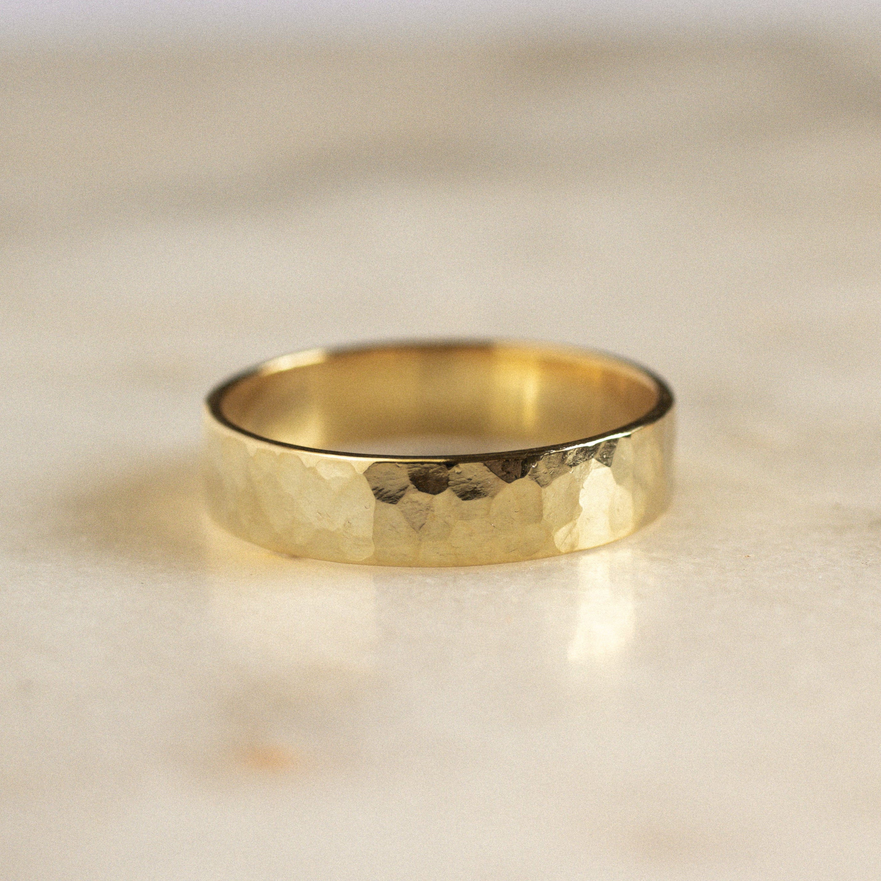 flat wide wedding ring in gold with chunky hammered wedding ring on marble surface