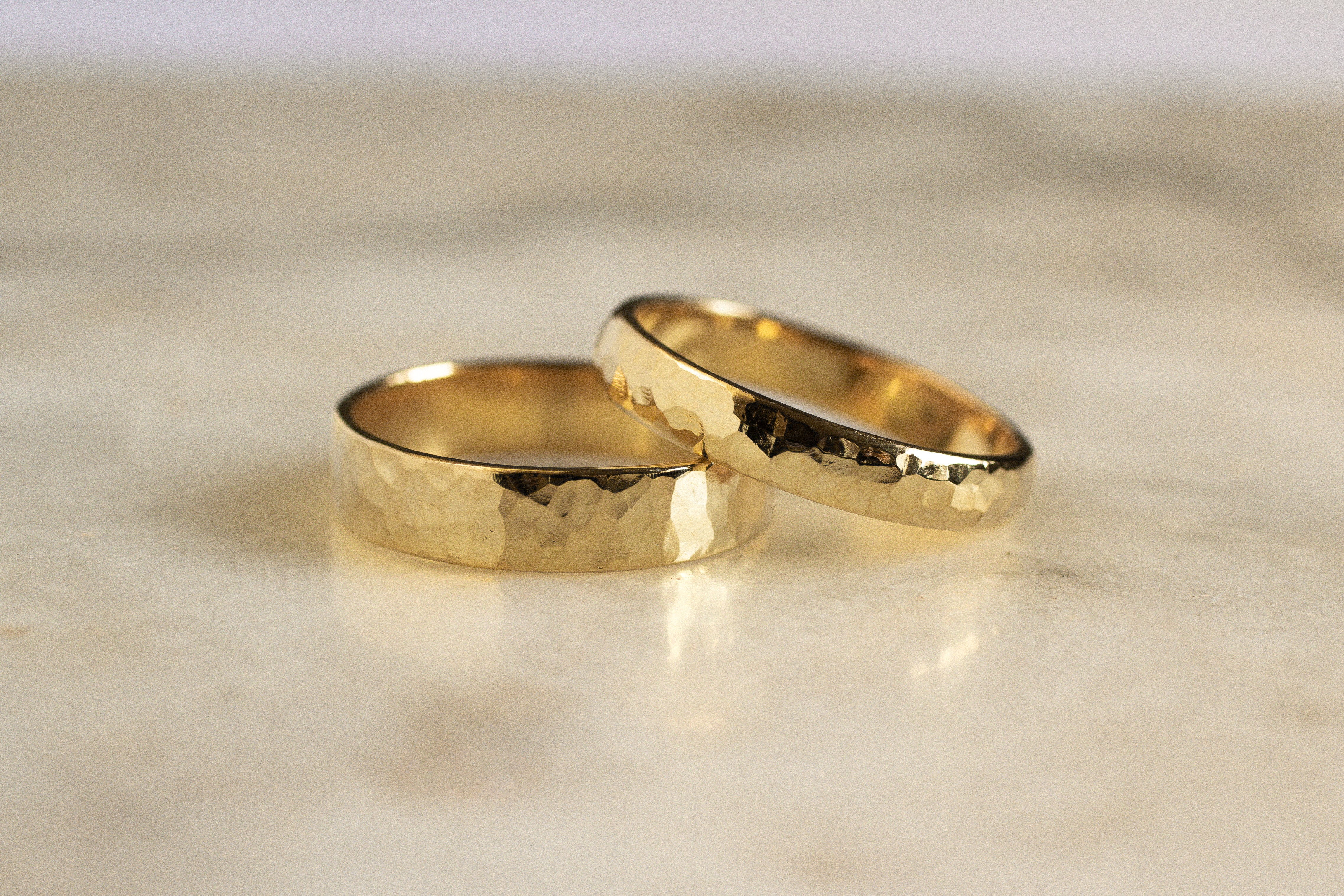 two gold wedding rings with chunky hammered texture on a marble surface