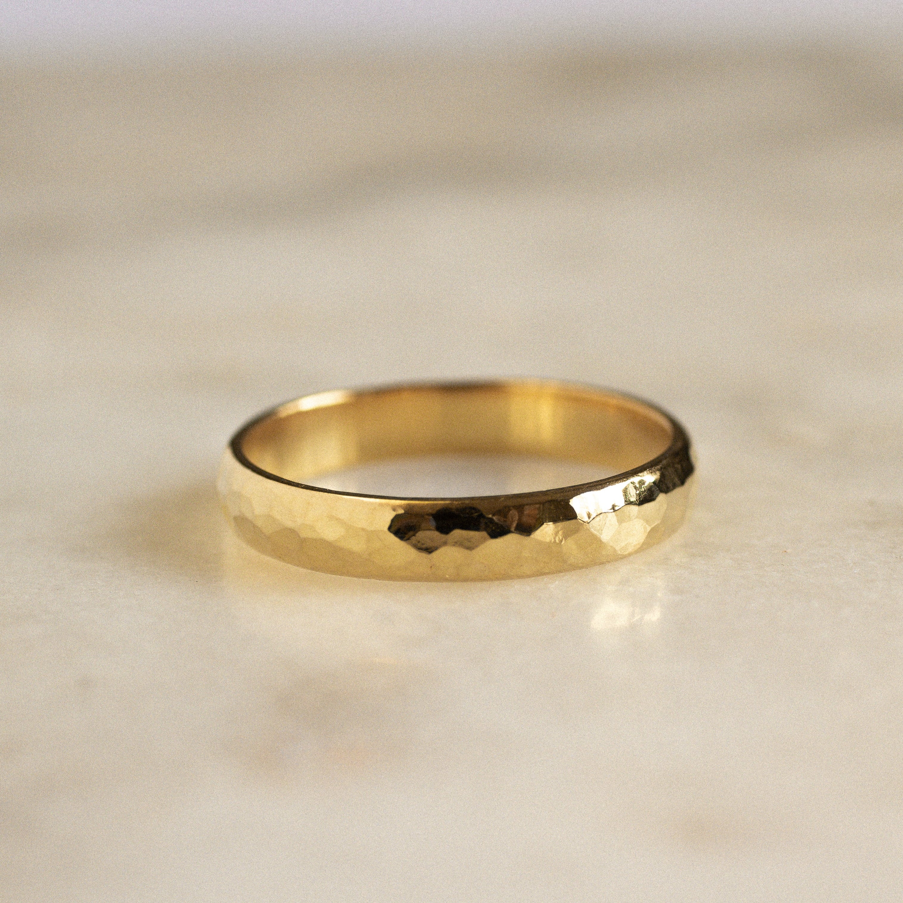 gold wedding ring with rounded edges and chunky hammered texture on marble surface