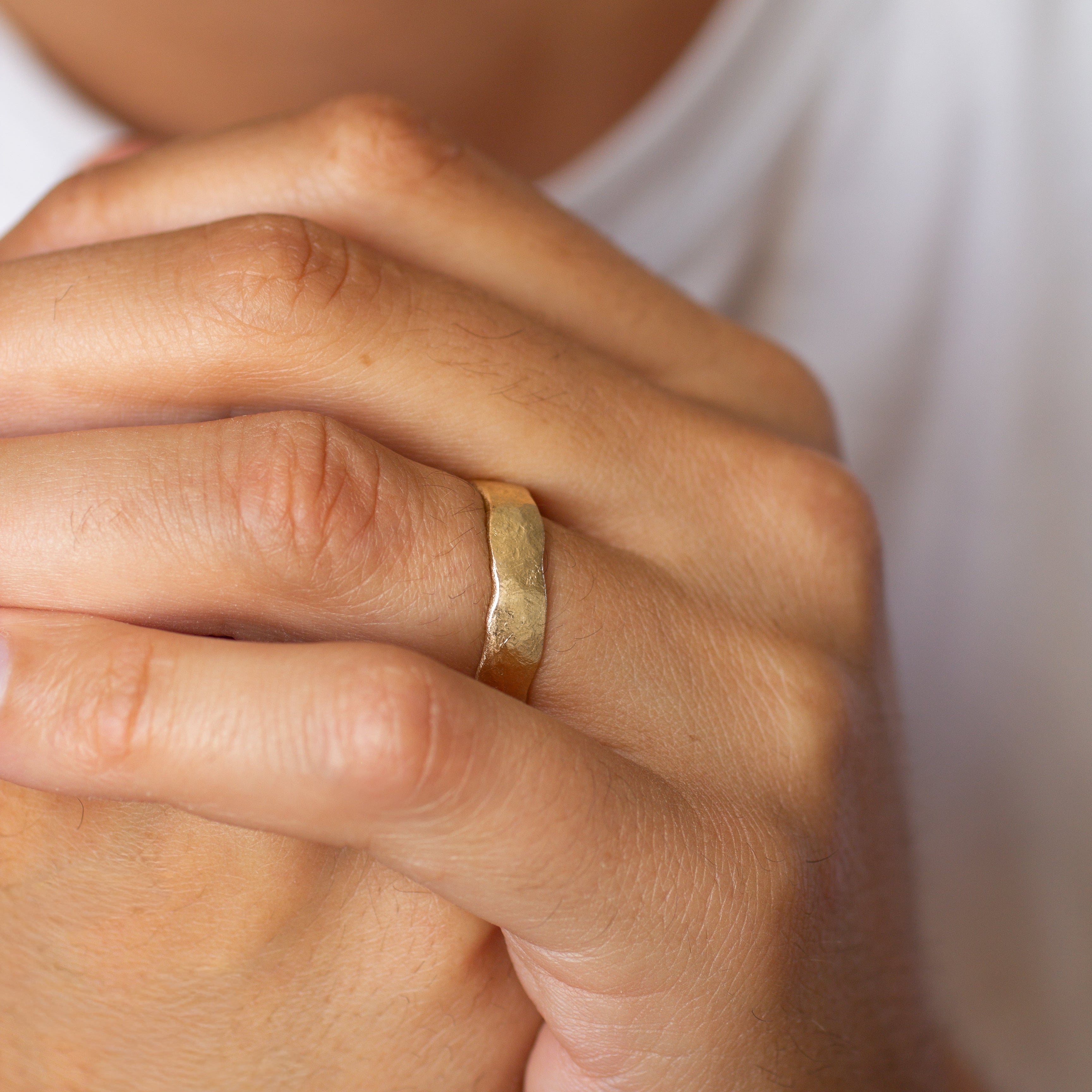 Close-up of a male hand wearing a gold rustic wedding ring with a blurred background