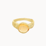 A textured gold signet ring with a smooth, oval, pale yellow gemstone, shown against a plain off-white background.