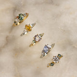 colourful engagement rings with green, yellow, pink and blue sapphires and diamonds on marble surface