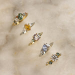 colourful engagement rings with green, yellow, pink and blue sapphires and diamonds on marble surface