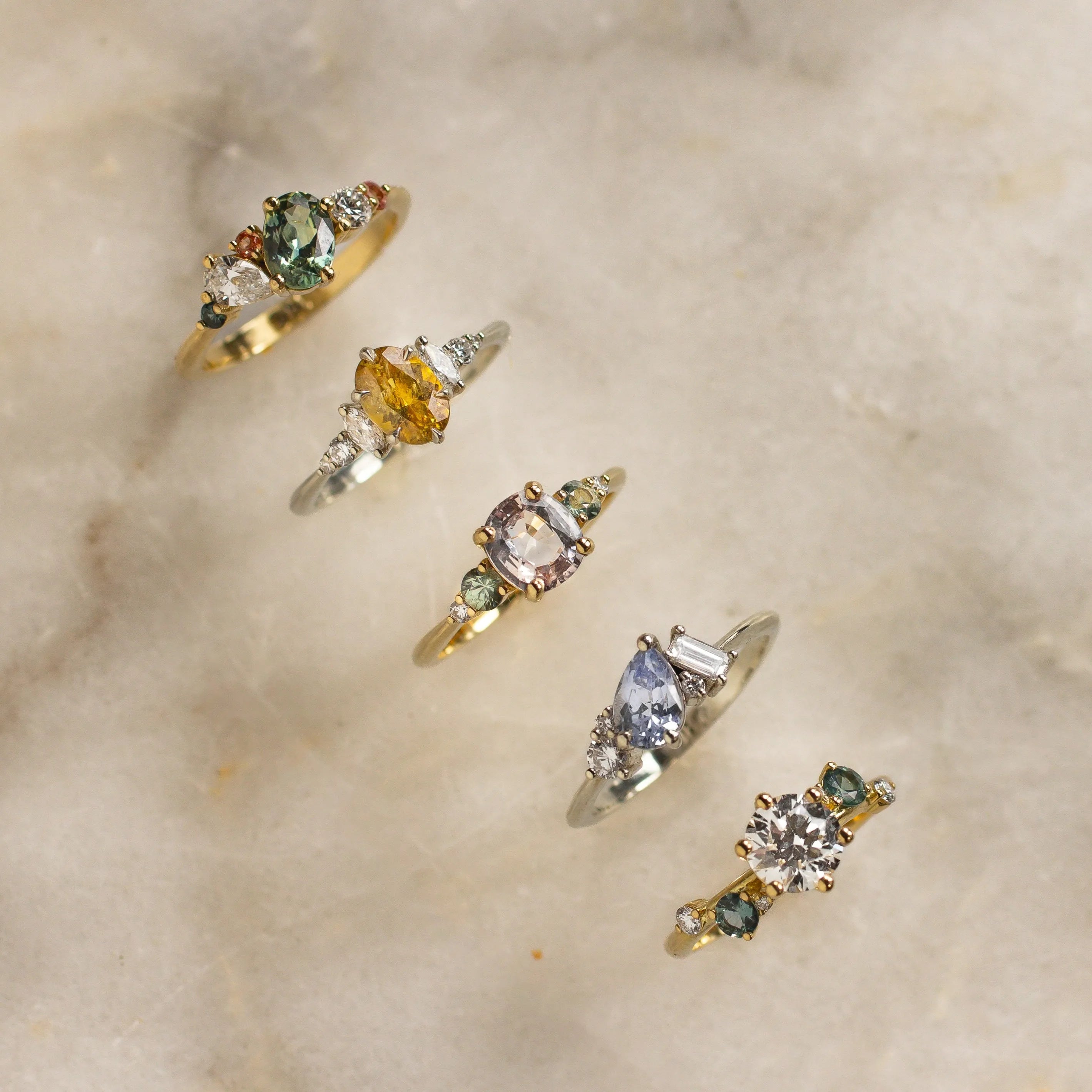colourful engagement rings with green, yellow, pink and blue sapphires and diamonds on marble surface