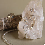 sun and moon dangle earrings on a white crystal with bead necklace with blurred sage and ring in the background