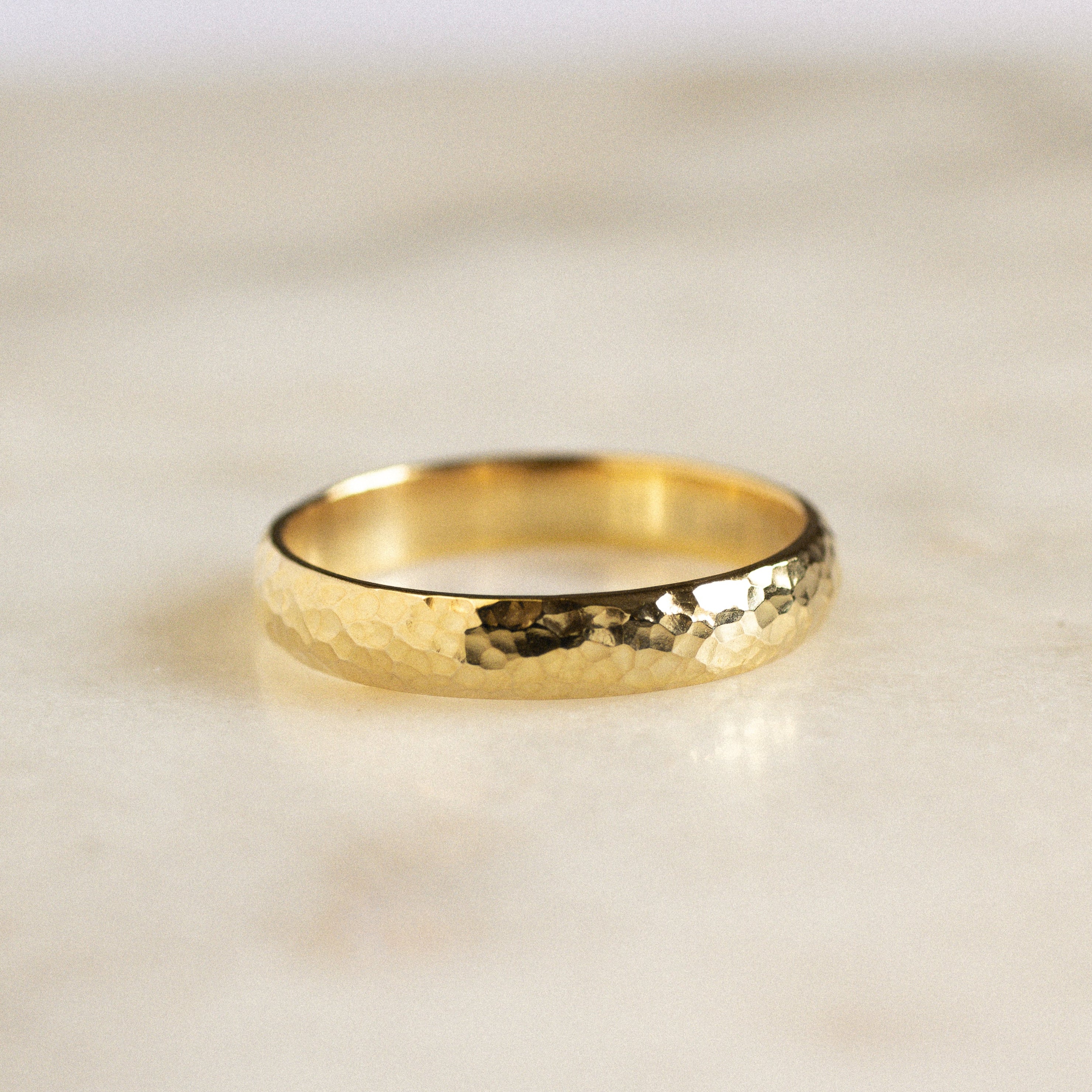 rounded gold wedding ring with dainty hammered effect on marble surface