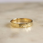 gold 3mm flat wedding ring with dainty hammered texture on marble surface 