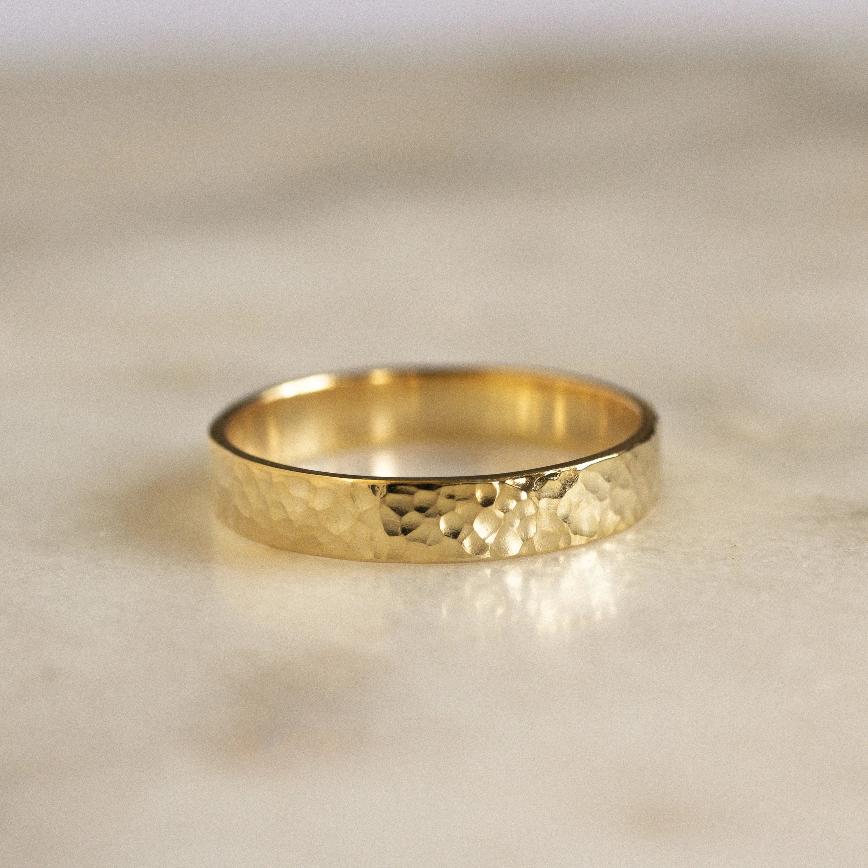 gold 3mm flat wedding ring with dainty hammered texture on marble surface 