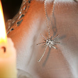 dandelion necklace in silver on neutral fabric with a blurred candle in the foreground