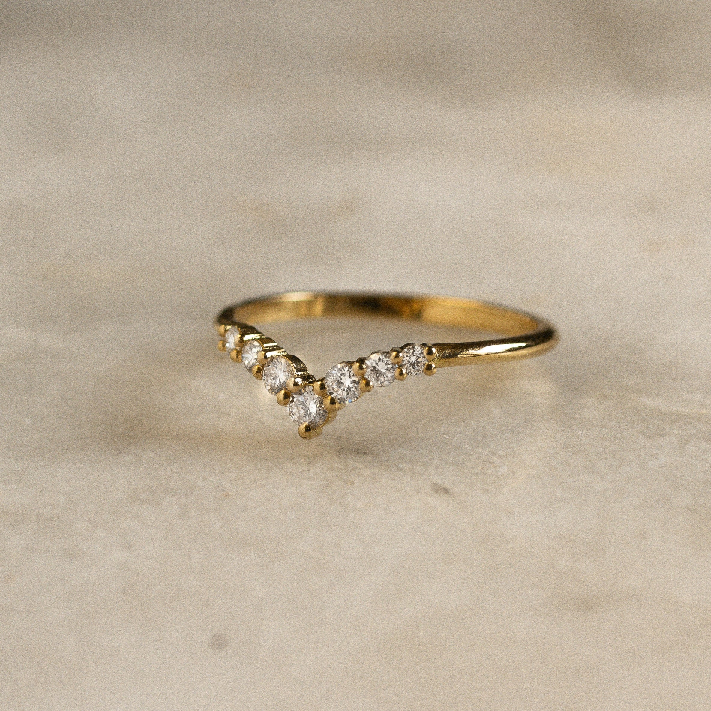 yellow gold chevron shaped wedding ring with 7 round diamonds on marble surface