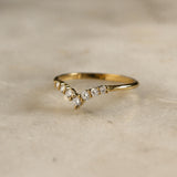 yellow gold chevron shaped wedding ring with 7 round diamonds on marble surface