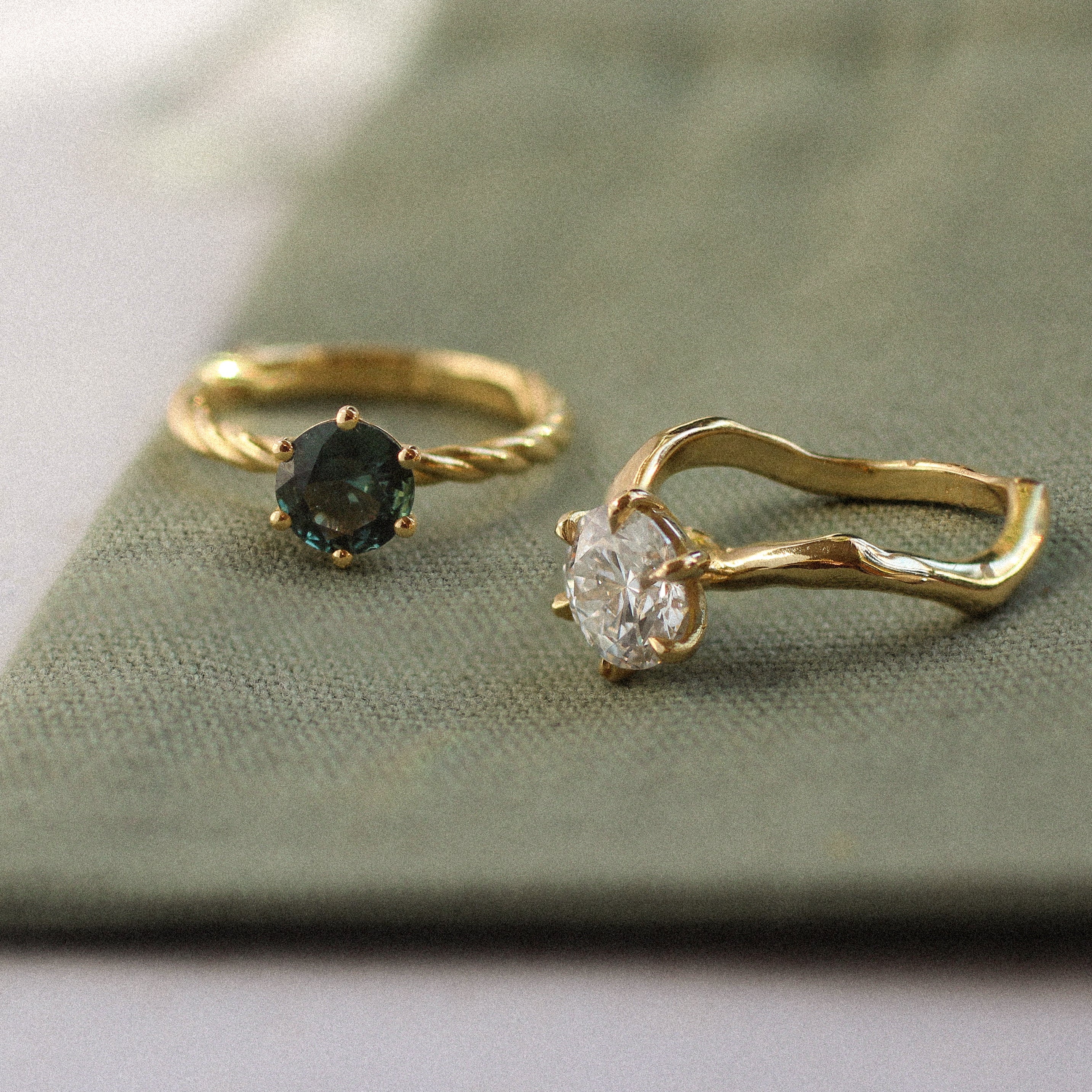 Two solitaire engagement rings with gemstones on a green fabric background