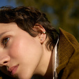 Close-up of a person wearing 2mm and 3mm diamond studs, a brown jacket with a blurred natural background