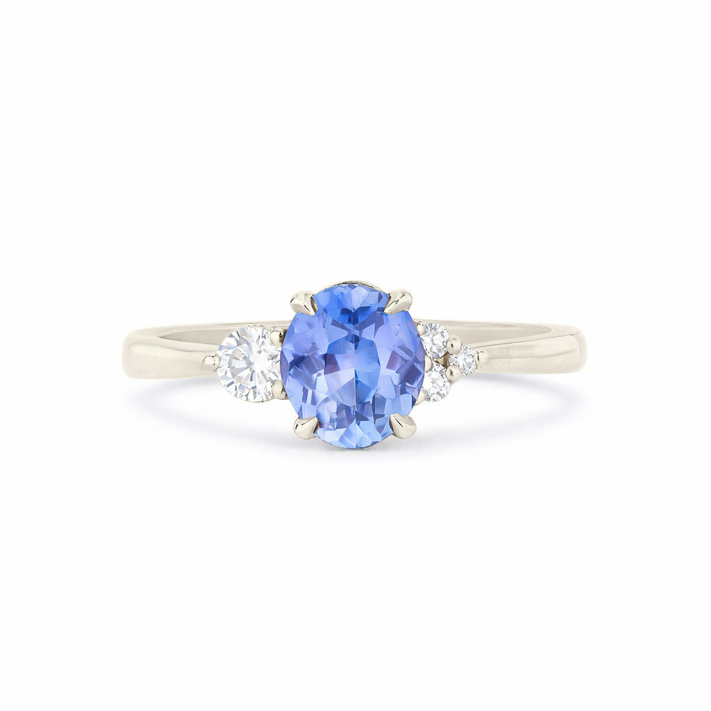 A three-stone diamond ring featuring a central oval-cut blue sapphire with round-cut diamonds on either side, set in a polished white gold band against a plain white background.