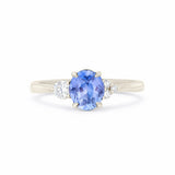 A three-stone diamond ring featuring a central oval-cut blue sapphire with round-cut diamonds on either side, set in a polished white gold band against a plain white background.