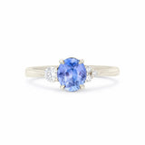 A three-stone diamond ring featuring a central oval-cut blue sapphire with round-cut diamonds on either side, set in a polished white gold band against a plain white background.
