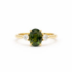 Gold engagement ring with a forest green sapphire and two smaller diamonds on a white background