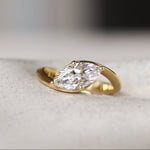 Gold curved engagement ring with a marquise diamond on a white ceramic dish