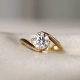 Gold engagement ring with a round diamond and curved wave shank on a textured surface