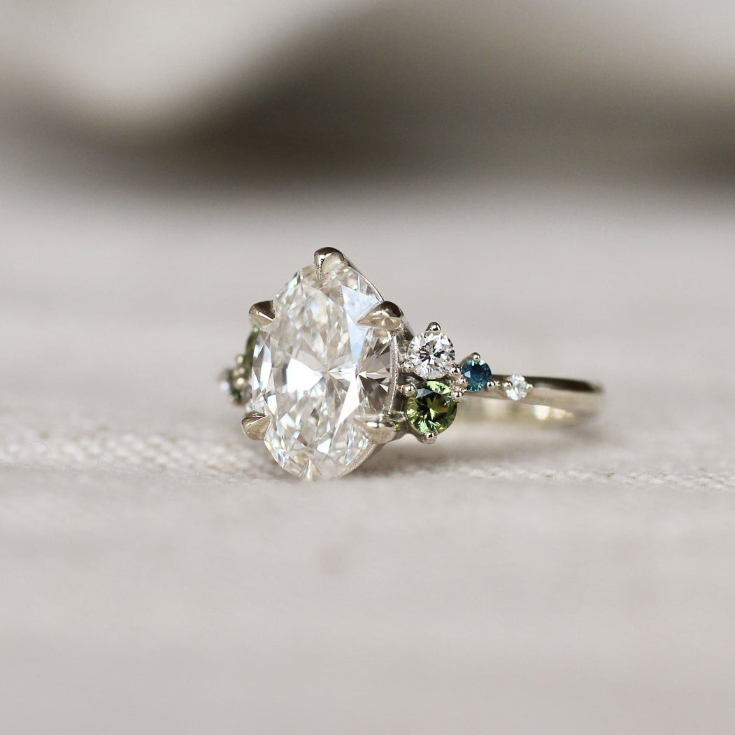 Diamond engagement ring in white gold with a small green and blue gemstones on a light background