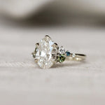 Diamond engagement ring in white gold with a small green and blue gemstones on a light background