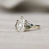 Diamond engagement ring in white gold with a small green and blue gemstones on a light background