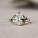 Large oval diamond ring with small green and blue gemstones on a textured surface
