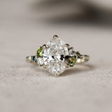 Large oval diamond ring with small green and blue gemstones on a textured surface