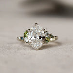 Large oval diamond ring with small green and blue gemstones on a textured surface