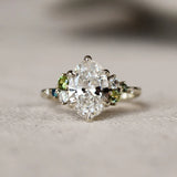 Large oval diamond ring with small green and blue gemstones on a textured surface