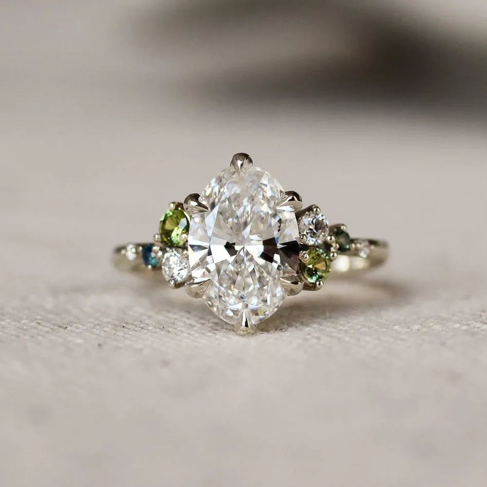Large oval diamond ring with small green and blue gemstones on a textured surface