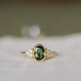 gold ring with oval bezel set sapphire and a cluster of 3 round diamonds either side with a blurred background