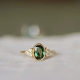 gold ring with oval bezel set sapphire and a cluster of 3 round diamonds either side with a blurred background