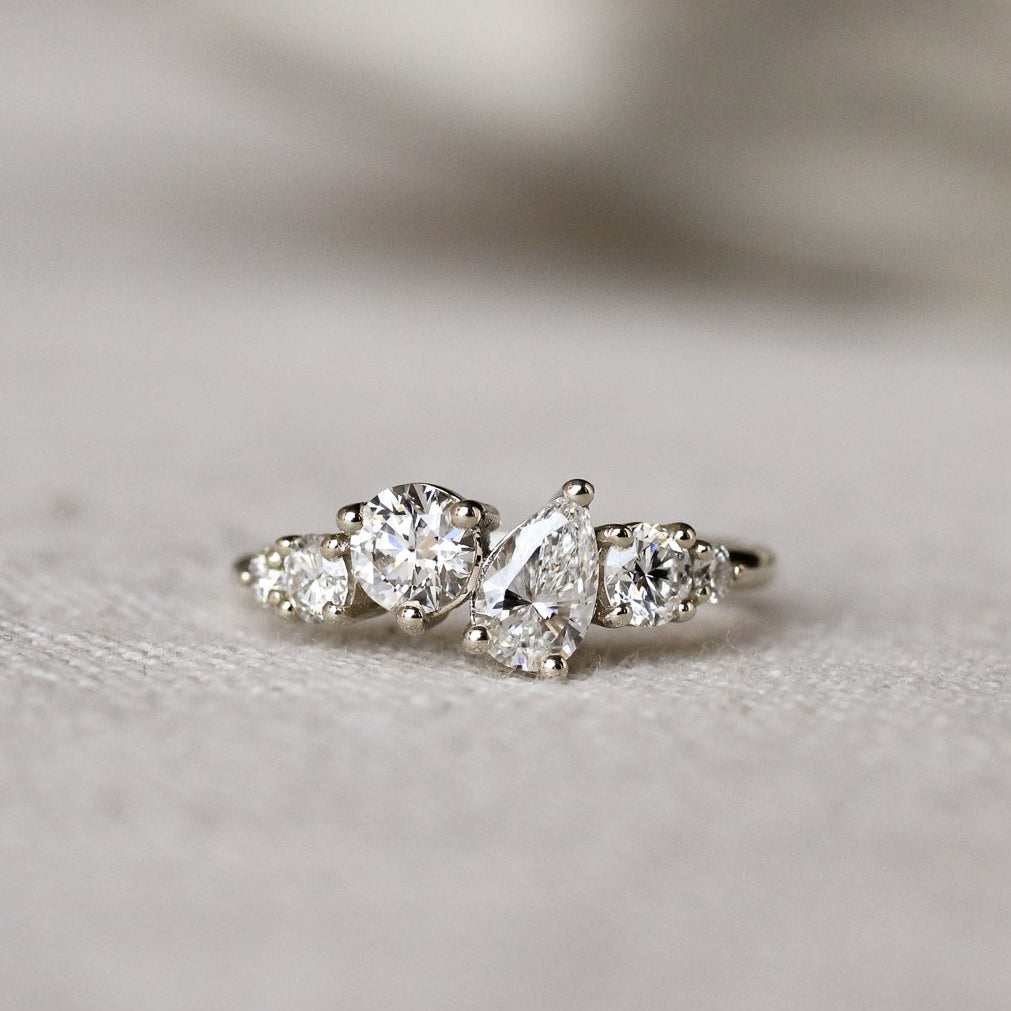Diamond ring with round and pear diamonds in an asymmetric ensemble on a textured surface with a blurred background
