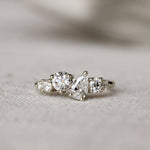 Diamond ring with round and pear diamonds in an asymmetric ensemble on a textured surface with a blurred background