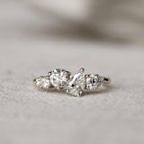 Diamond ring with round and pear diamonds in an asymmetric ensemble on a textured surface with a blurred background