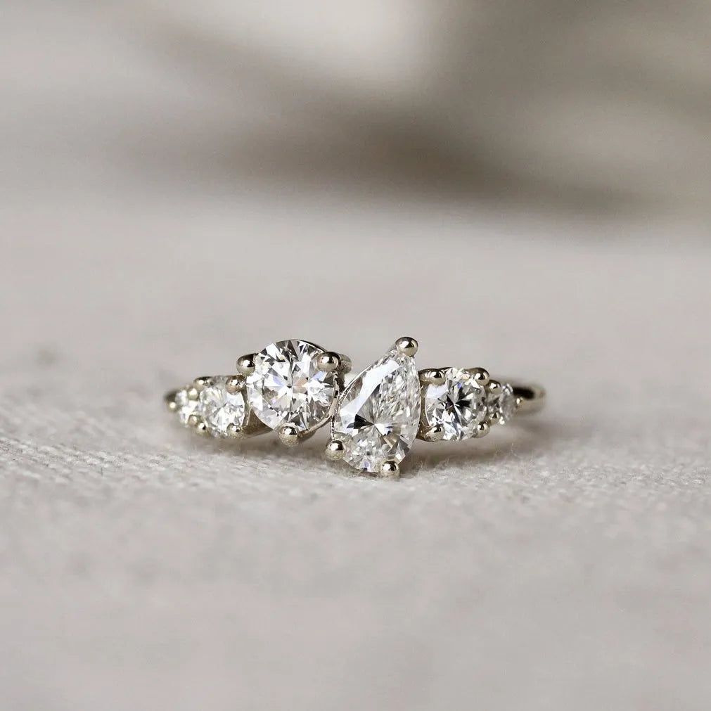 Diamond ring with round and pear diamonds in an asymmetric ensemble on a textured surface with a blurred background