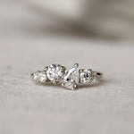 Diamond ring with round and pear diamonds in an asymmetric ensemble on a textured surface with a blurred background