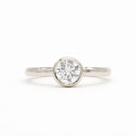 A white-gold solitaire engagement ring with a round brilliant-cut diamond set in a bezel setting, shown on a clean white background.