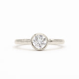 A white-gold solitaire engagement ring with a round brilliant-cut diamond set in a bezel setting, shown on a clean white background.