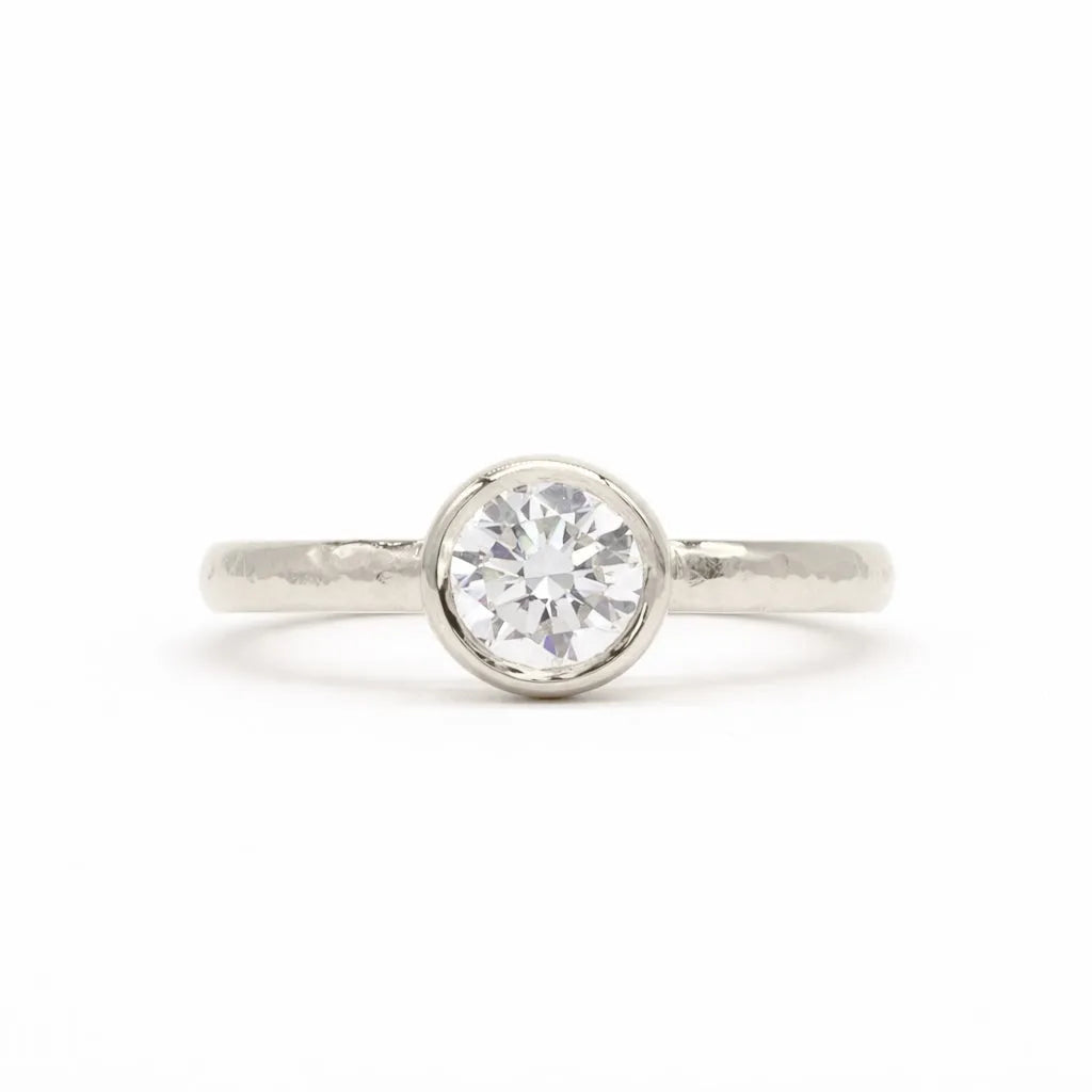 A white-gold solitaire engagement ring with a round brilliant-cut diamond set in a bezel setting, shown on a clean white background.