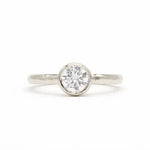A white-gold solitaire engagement ring with a round brilliant-cut diamond set in a bezel setting, shown on a clean white background.