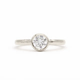 A white-gold solitaire engagement ring with a round brilliant-cut diamond set in a bezel setting, shown on a clean white background.
