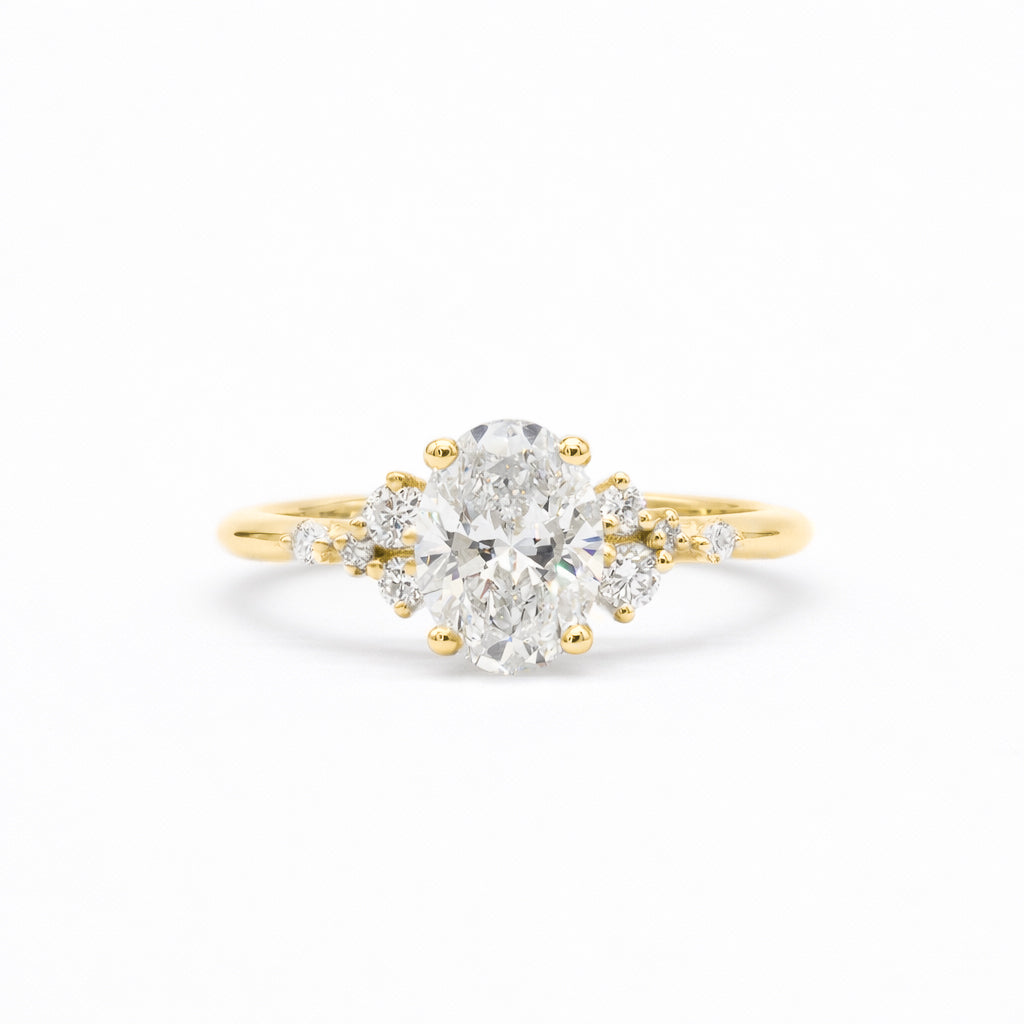 A yellow gold ring featuring a large oval-cut center diamond surrounded by smaller round diamonds on the shoulders, set against a clean white background.
