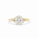 A yellow gold ring featuring a large oval-cut center diamond surrounded by smaller round diamonds on the shoulders, set against a clean white background.